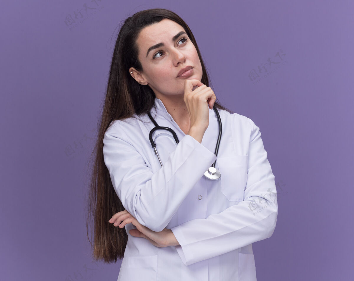 年轻体贴的年轻女医生穿着带听诊器的医用长袍抬起下巴持有医学穿