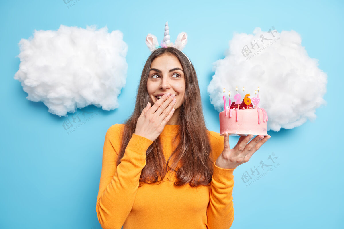 美味女人在庆祝生日时手拿草莓蛋糕 嘴里咯咯笑着穿着蓝色的休闲套头衫头带火乐趣