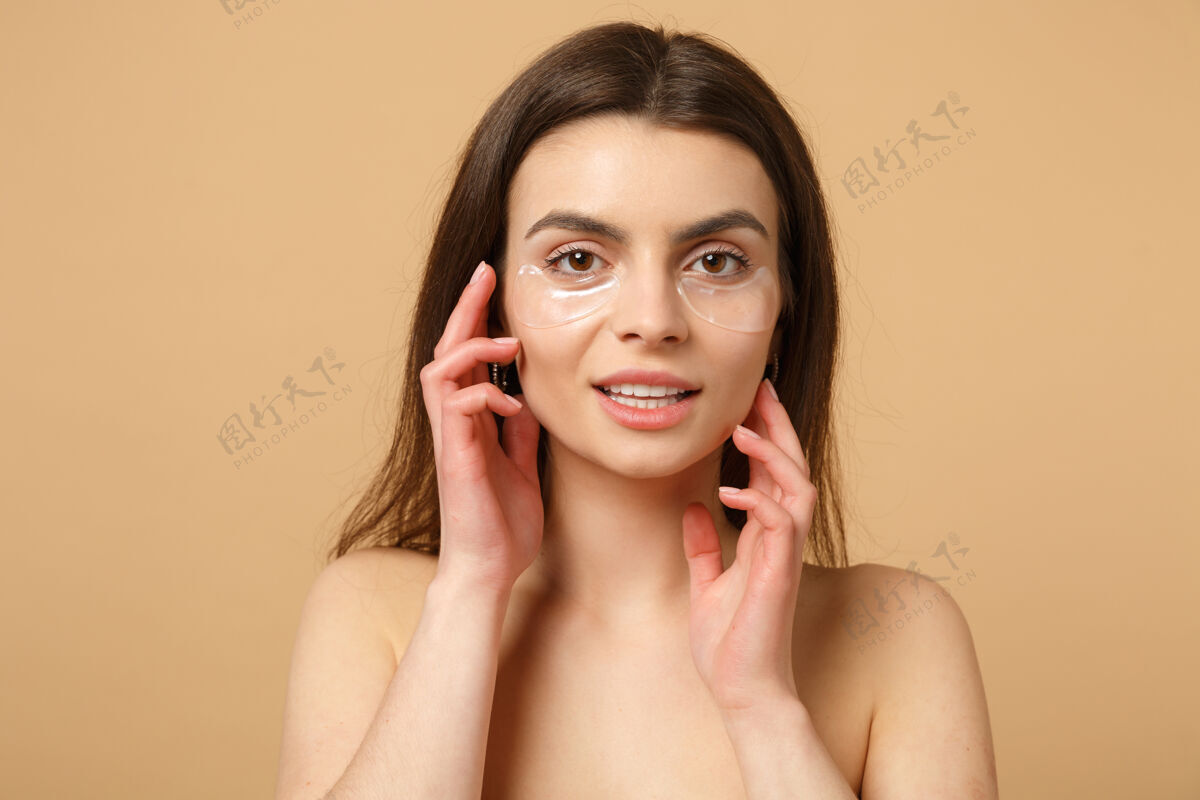 肩膀近距离拍摄完美皮肤的半裸女人 在米色粉彩墙上隔离眼睛下的裸妆贴片清晰皮肤补丁