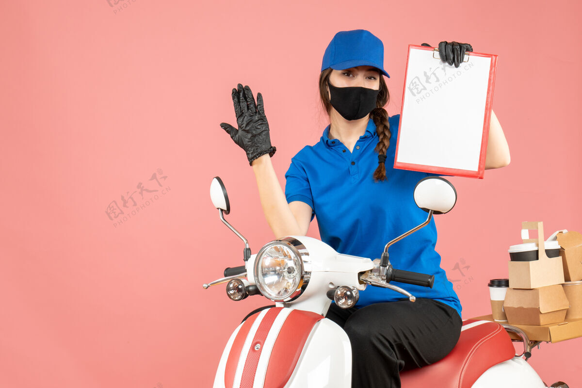 纸顶视图好奇的信使女孩戴着医用口罩和手套坐在滑板车上拿着空纸在粉彩桃色背景下传递订单床单背景摩托车
