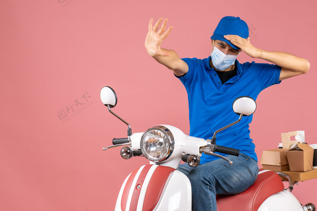 球员顶视图：戴着医用面罩 戴着帽子的送货员坐在滑板车上 在粉彩桃子上做着停车手势体育使男性