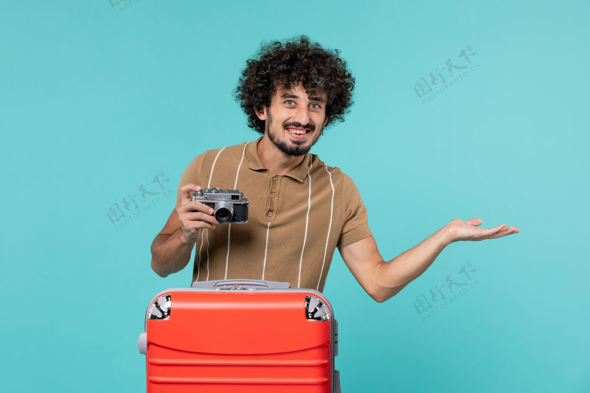 旅行带着红色手提箱的度假男人用相机在蓝色上微笑拍照旅行拍摄手提箱