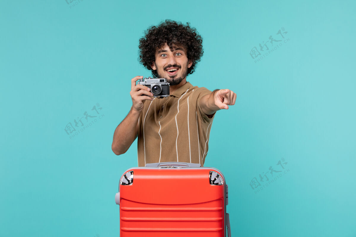 男人带着红色手提箱的度假男人用淡蓝色的相机拍照包人红色