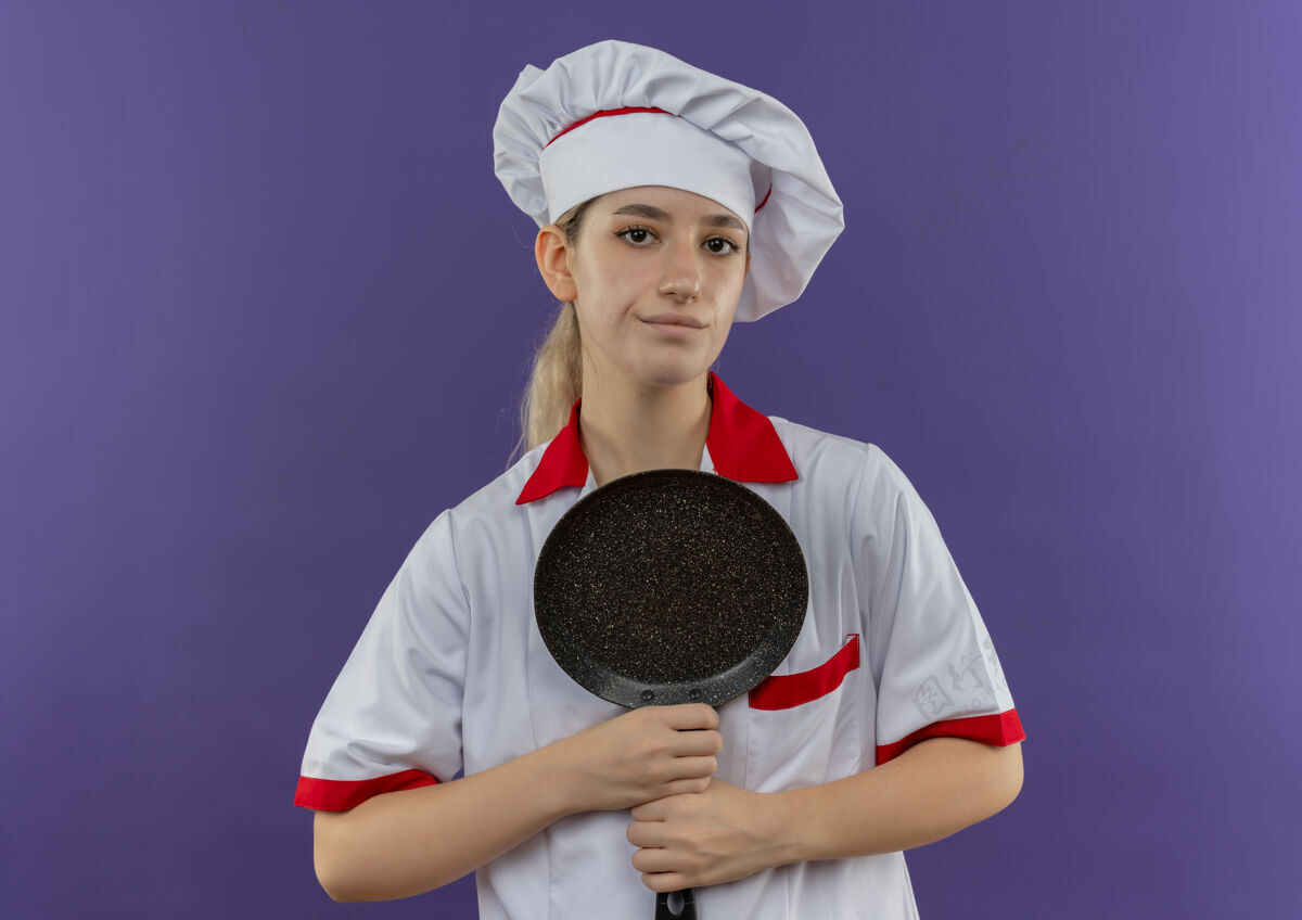 年轻自信的年轻漂亮厨师 身着厨师制服 手拿煎锅 在紫色的墙上显得孤立无援厨师烹饪薯条