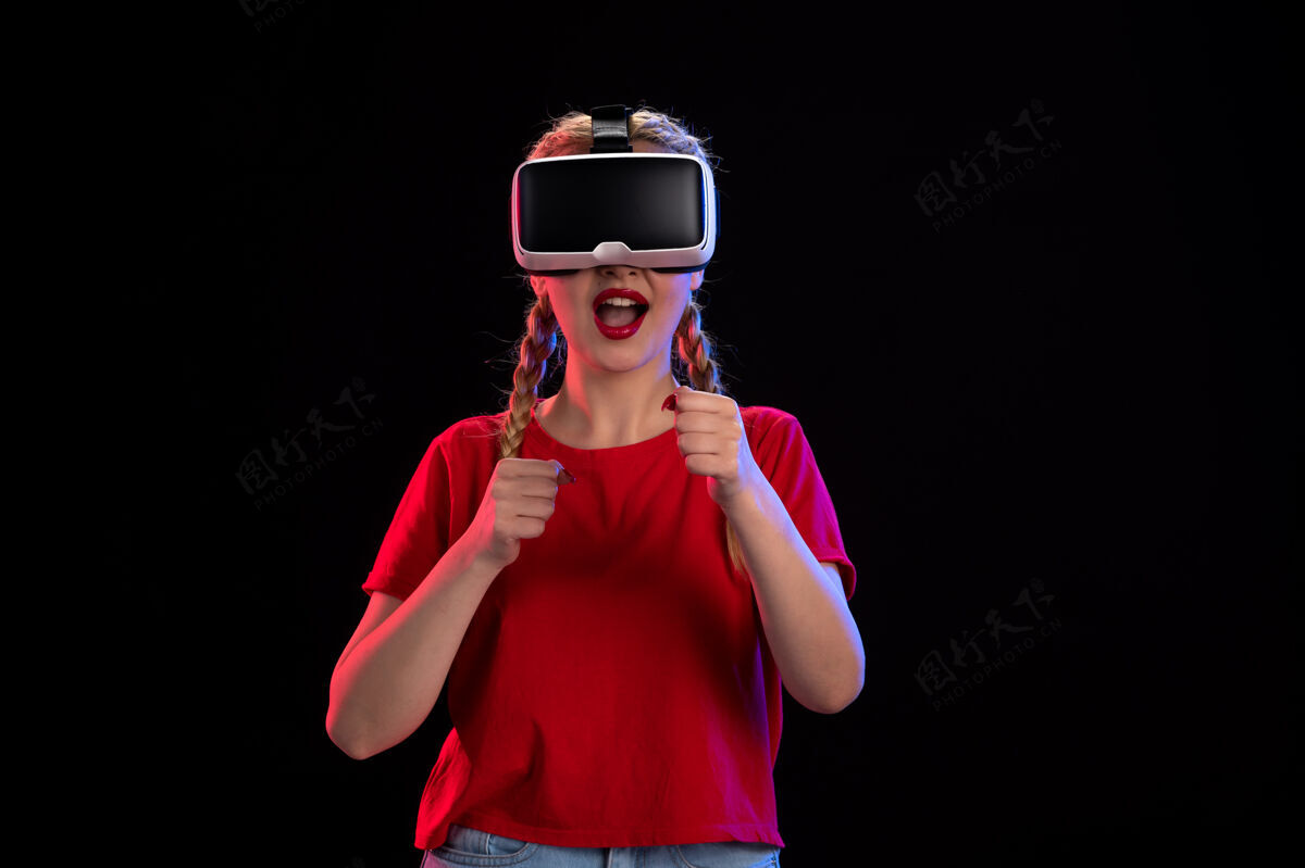 正面年轻女性在黑暗的墙上玩虚拟现实的正面图肖像表情护目镜