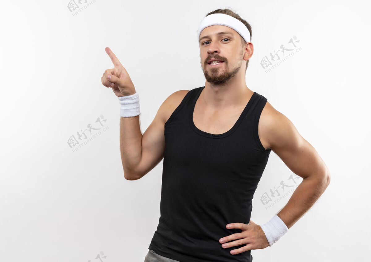 男人自信的年轻帅气的运动型男人戴着头带和腕带 手放在腰上 隔离在白色墙壁上 留有复制空间年轻穿运动