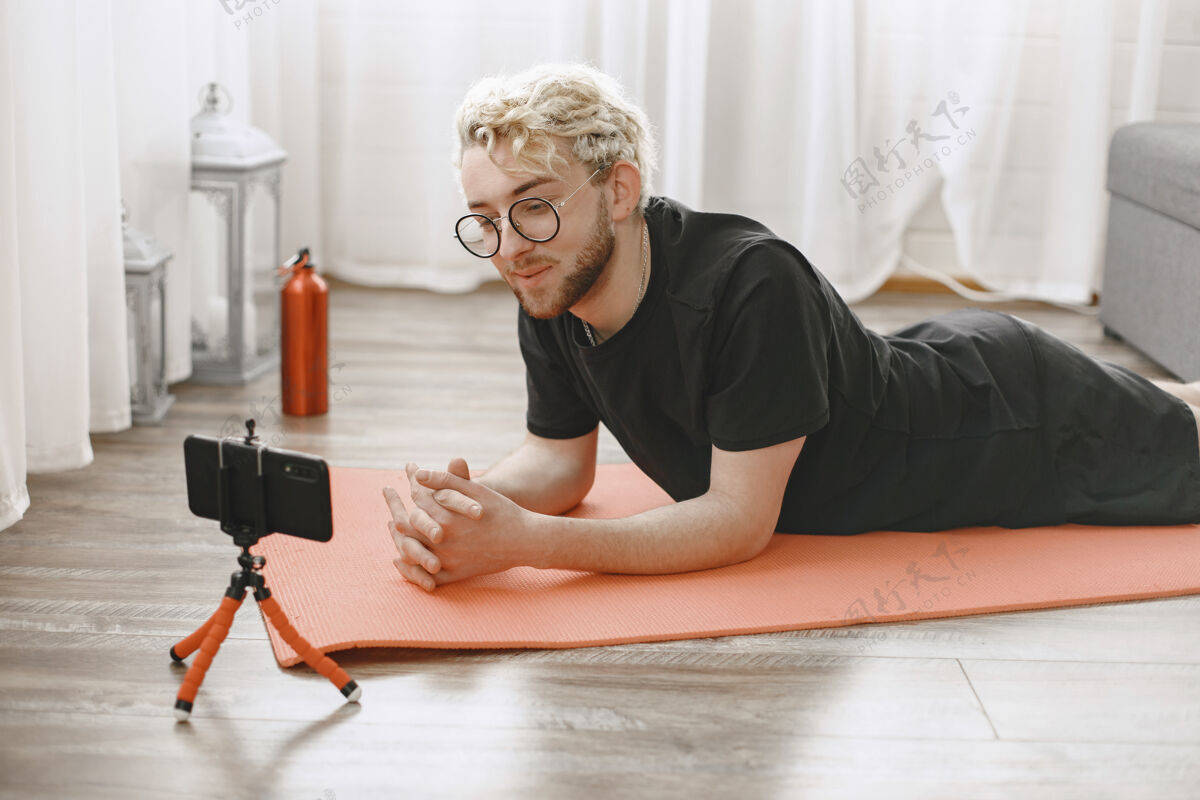 移动健身教练或视频博主在做伸展运动这名男子正在家里用智能手机摄像头拍摄自己普拉提公寓健身