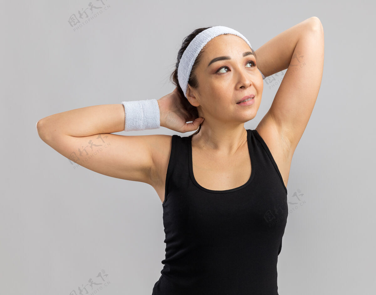 伸展戴着头巾的年轻健身女士站在白色的墙上 向一边伸展双手准备锻炼健身靠边手