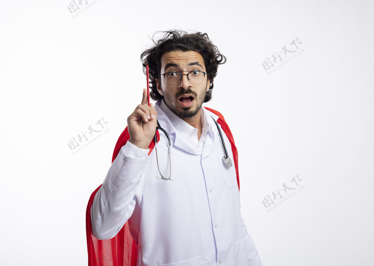 眼镜令人印象深刻的年轻白种人超级英雄戴着眼镜 身穿医生制服 披着红色斗篷 脖子上戴着听诊器 手里拿着铅笔穿复制铅笔