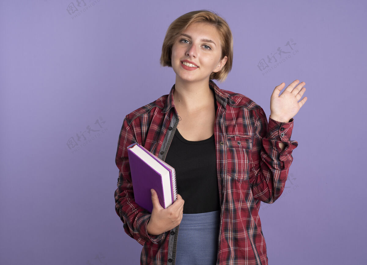举起微笑着的年轻斯拉夫女学生举起手站着 手里拿着书和笔记本复制手斯拉夫