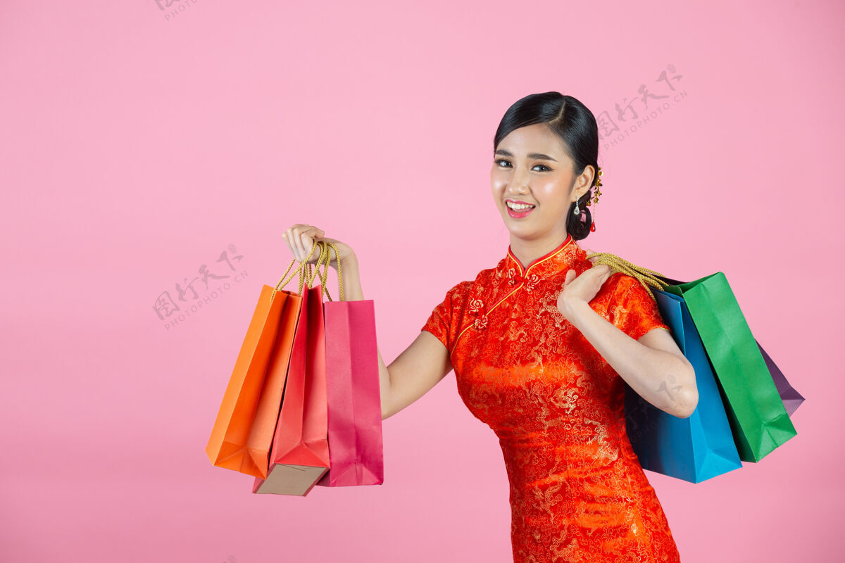 展示美丽的亚洲女人快乐的微笑和购物在中国新年的粉红色背景东方红色购物
