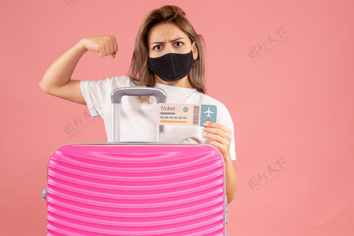 粉红色一个戴着黑色面具的强壮的年轻女子拿着票站在粉红色的手提箱后面脸保护罩成人