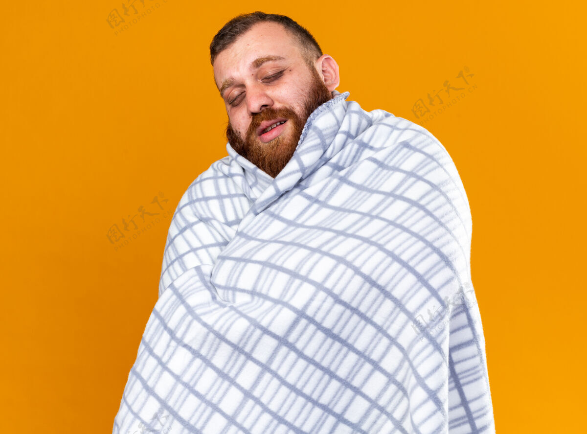 站不健康的胡子男人裹着毯子 感觉不舒服 站在橙色的墙上闭着眼睛 忍受着寒冷病痛苦冷