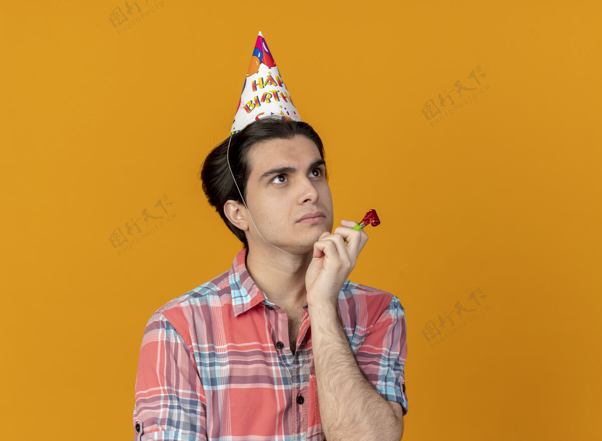 穿体贴帅气的白种人戴着生日帽 手放在下巴上 手持派对口哨 看着身边壁板下巴思想
