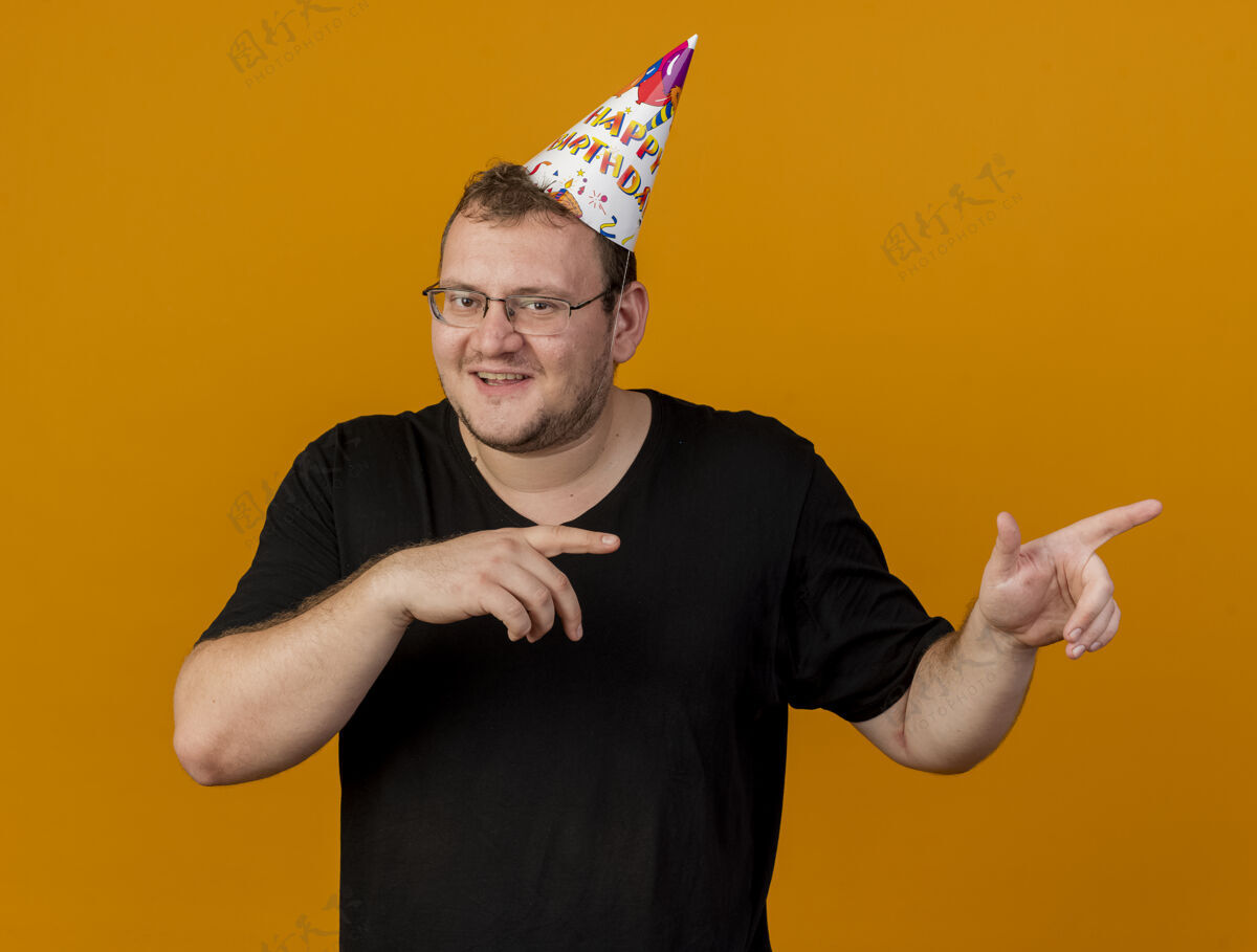 二高兴的成年斯拉夫男子戴着眼镜戴着生日帽 两手点在一旁点手光学
