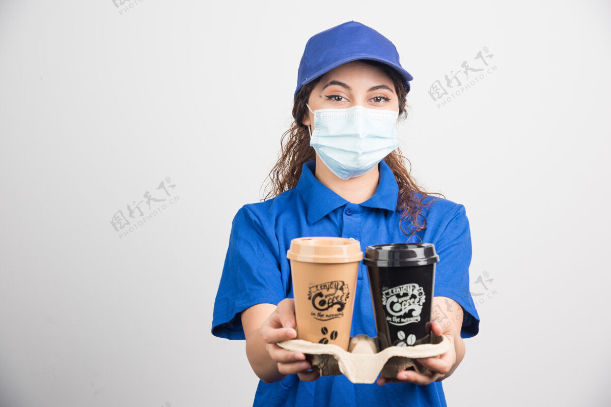 女性一个穿着蓝色制服 戴着医用口罩的女人 手里拿着两杯咖啡提供成人帽子