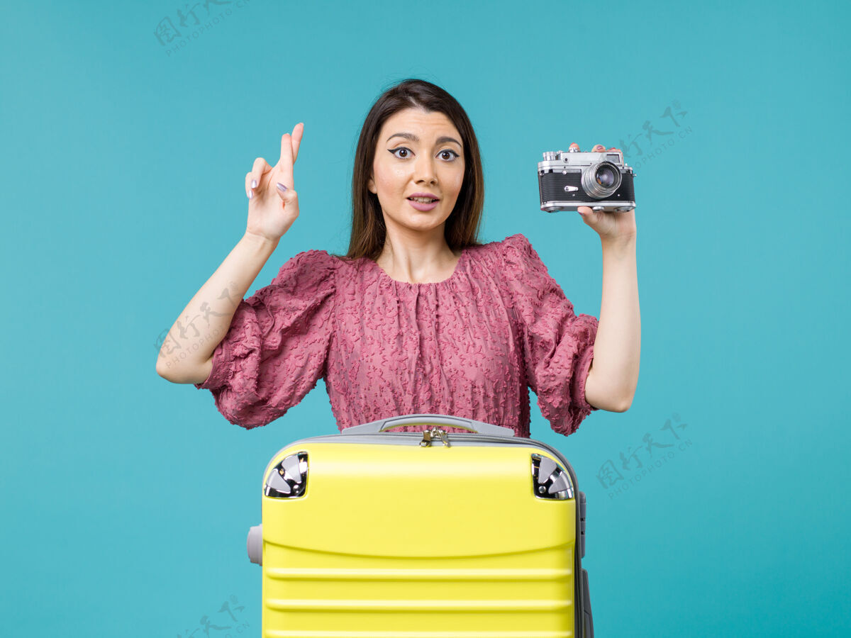人物前景度假中的年轻女子用相机在蓝色背景上拍照旅行海上旅行女子出国度假年轻女子肖像旅程