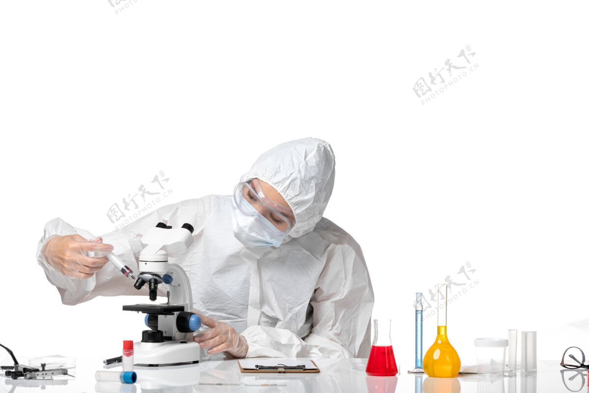 大流行正面图年轻女医生穿着白色防护服 戴着口罩 由于科维德在显微镜下工作 背景为浅白色病毒大流行 飞溅科维德-病毒年轻女医生专业