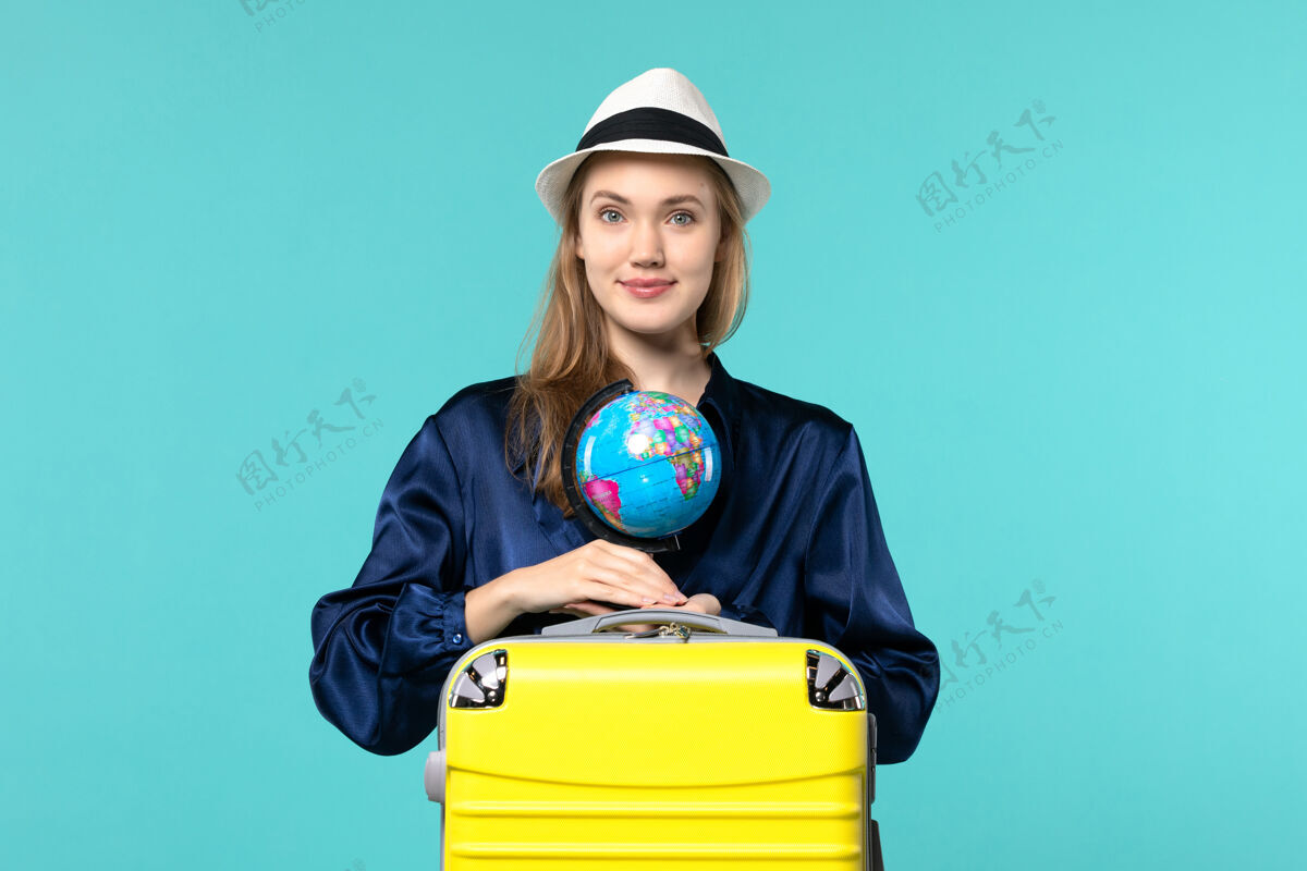 年轻女子正面图年轻女子手持地球仪 准备在蓝色背景飞机上度假女性度假之旅远航大海微笑航行举行