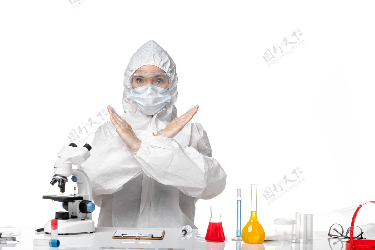专业正面图年轻女医生穿着白色防护服 带口罩 因covid显示禁止标志白色背景病毒大流行飞溅covid-表演口罩药品