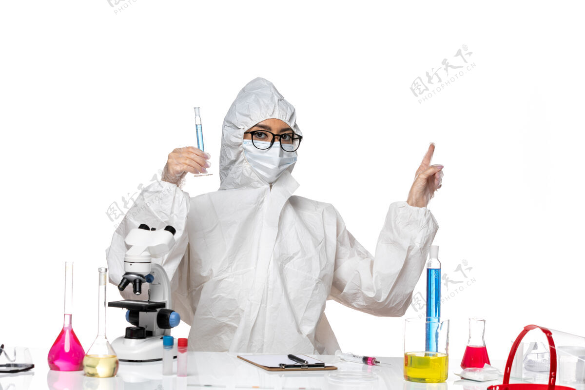 医疗正面图身穿特殊防护服的年轻女化学家拿着装有蓝色溶液的烧瓶 背景是白色的实验室冠状病毒化学病毒医药外套特殊