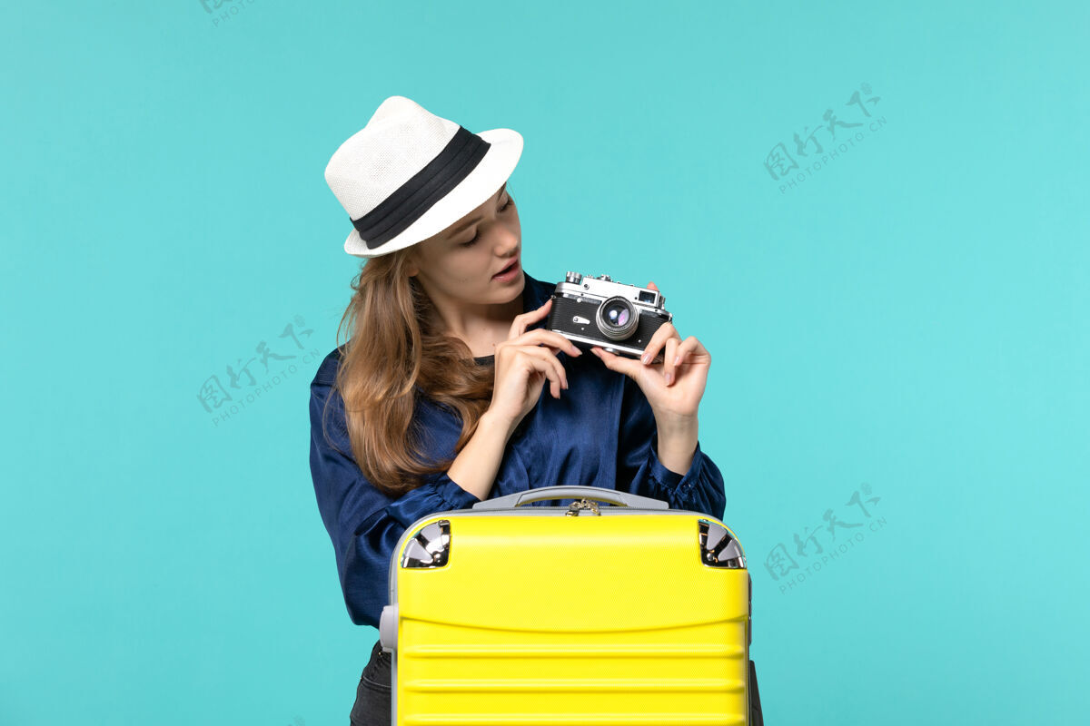 成人前视图年轻女子手持相机 在蓝色背景的女子海上旅行飞机上拍照女士摄影师旅行