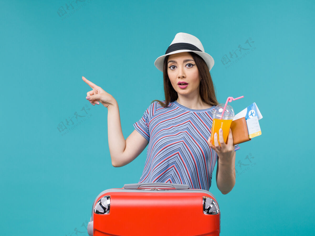 航行前景：度假中的女人拿着她的红包 手里拿着机票和果汁 坐在蓝色的办公桌上旅行 旅行 度假 女人旅行果汁微笑举行