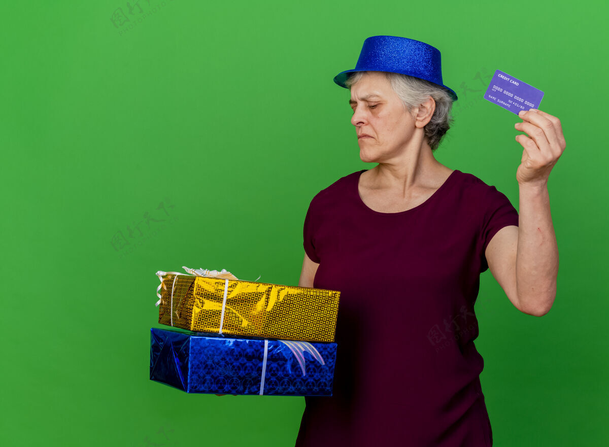 信用戴着派对帽的自信的老妇人拿着礼品盒和信用卡在绿色的草地上聚会老人信心