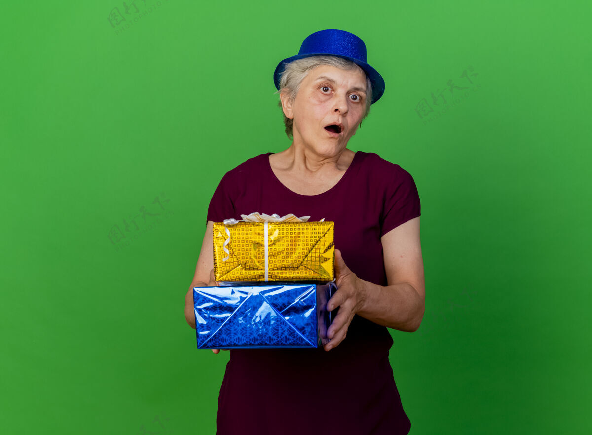 聚会戴着派对帽的震惊的老妇人拿着绿色的礼盒盒子女人帽子