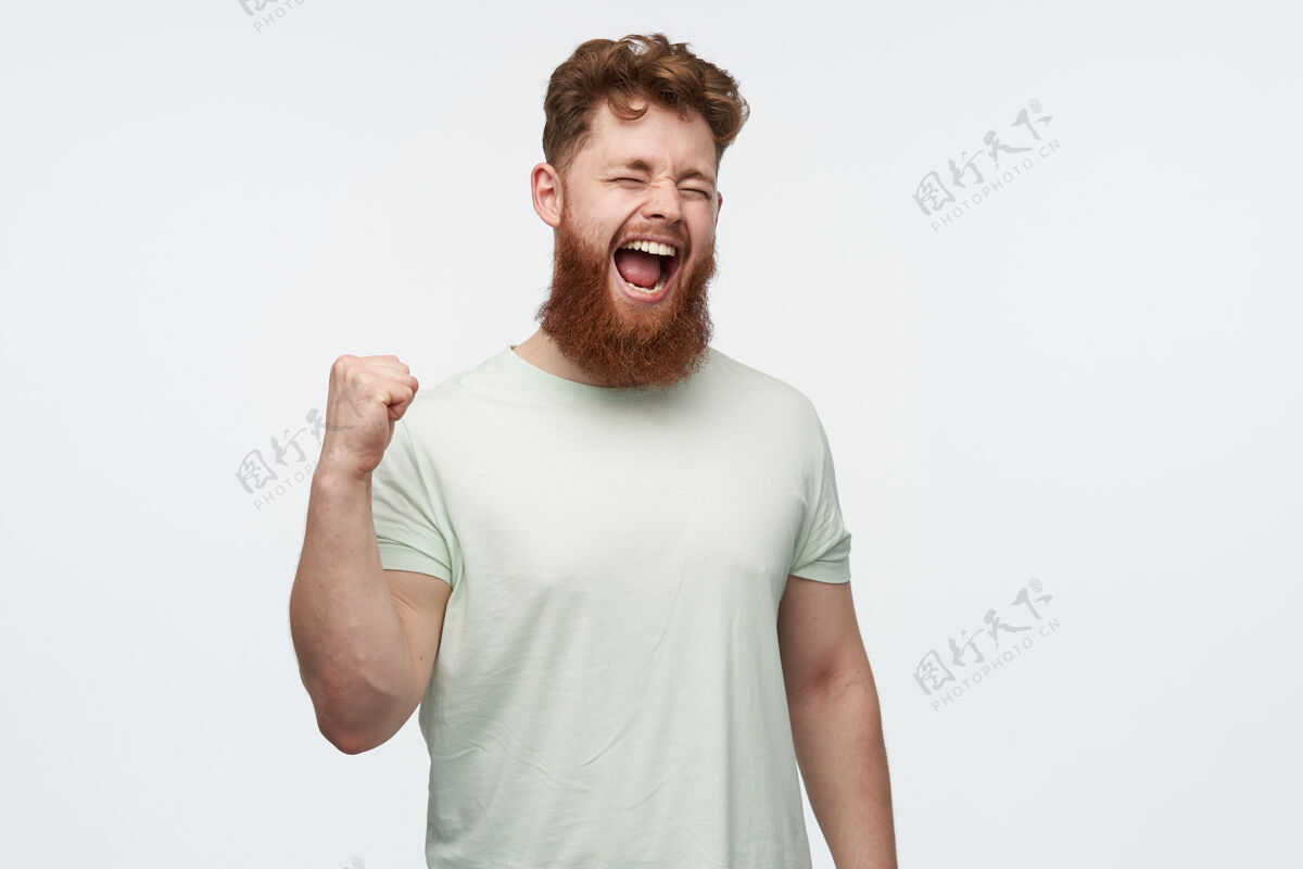 休闲年轻的红胡子男人的画像穿着一件空白的t恤 举起拳头 一边看足球比赛一边大喊大叫男人时尚模特