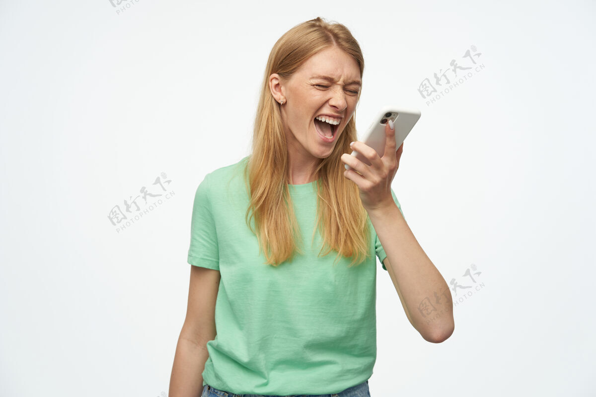 喊叫愤怒的疯女人 带着雀斑 穿着薄荷色T恤 一边用手机说话 一边用白色尖叫魅力雀斑姿势