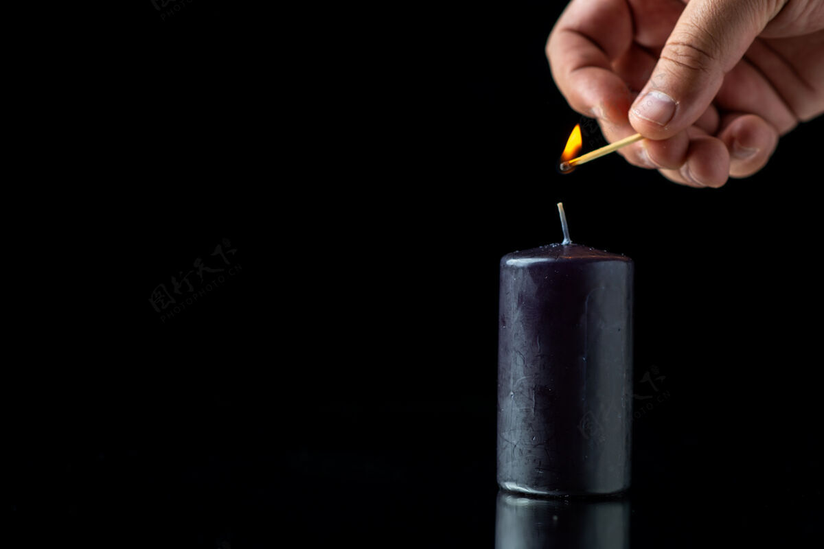 视图黑暗表面上黑蜡烛的正视图手指举行笔