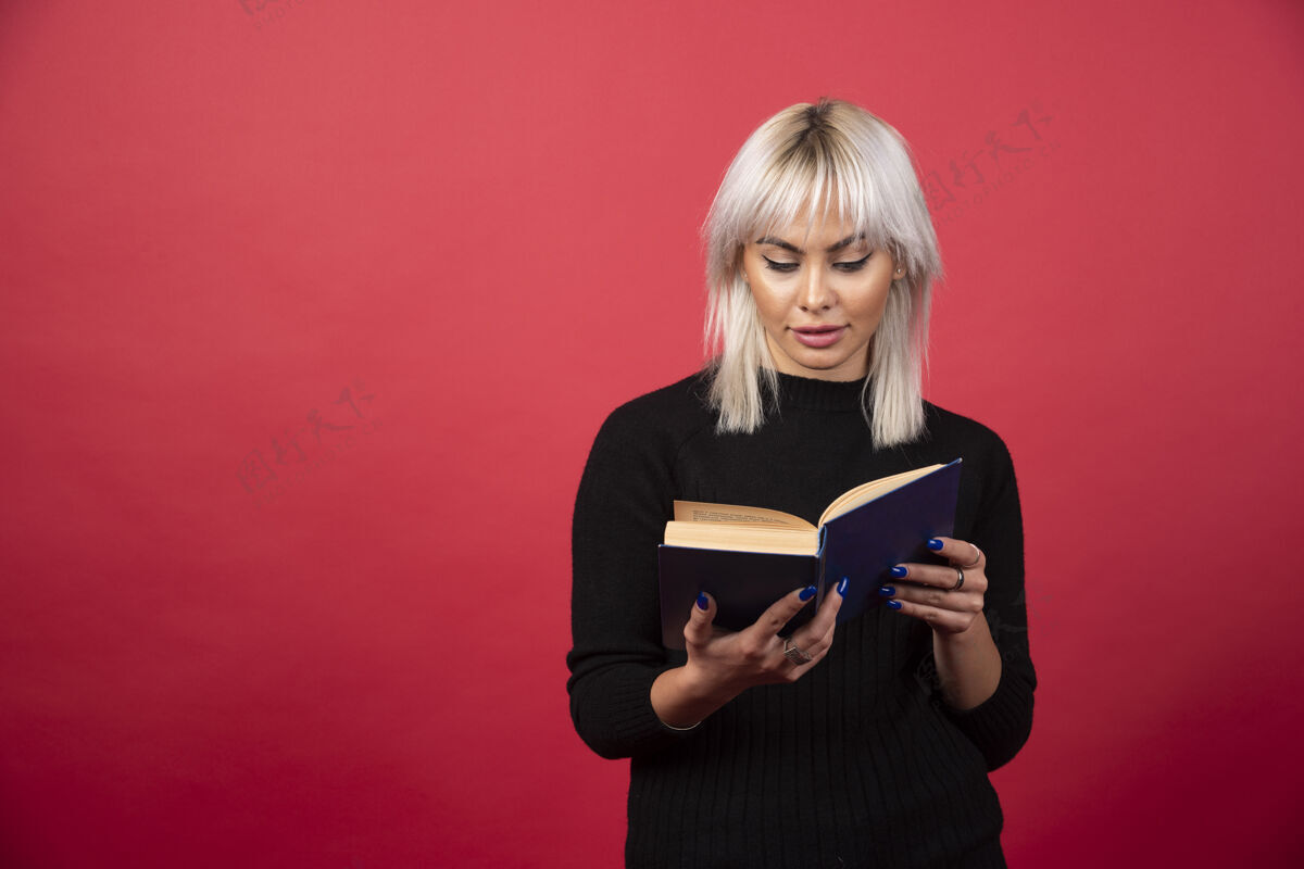 手持年轻的女模特正在阅读一本红色背景的书高质量的照片肖像青年明亮