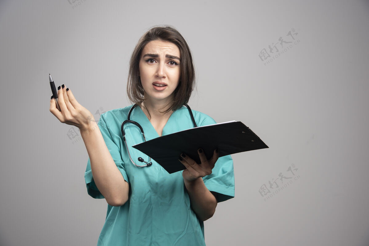 医生穿着蓝色制服的女医生拿着灰色背景的剪贴板高质量的照片疾病健康职业