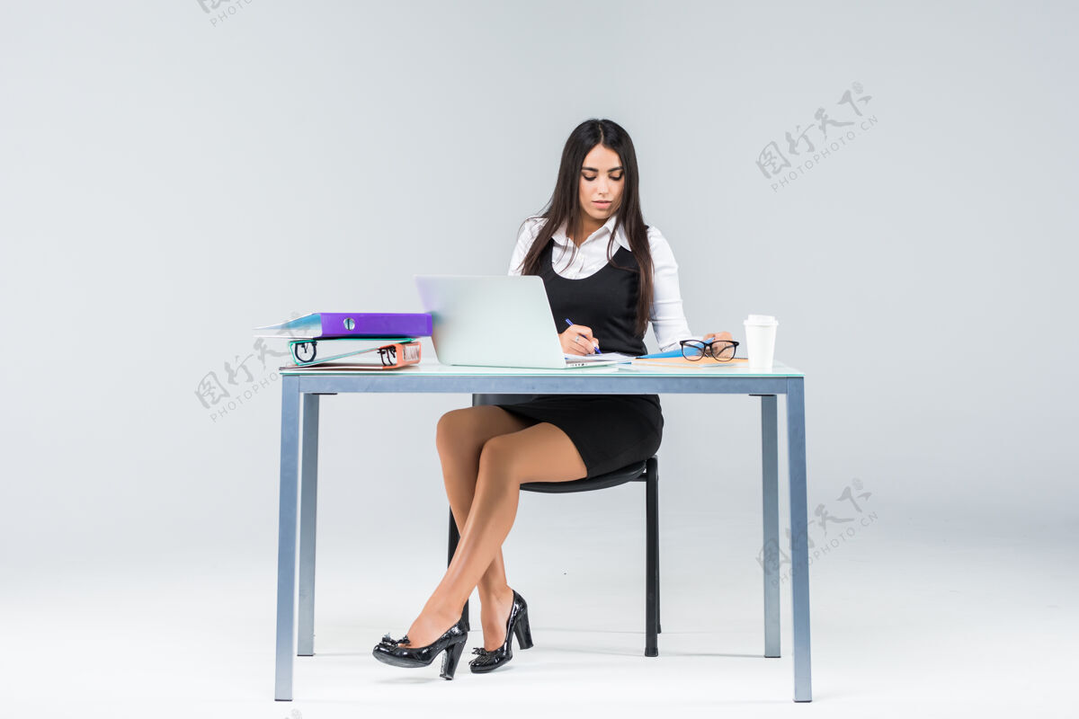 人年轻漂亮的女商人坐在工作台上工作 在纸和笔记本电脑上孤立的灰色行政人员笔记本电脑屏幕
