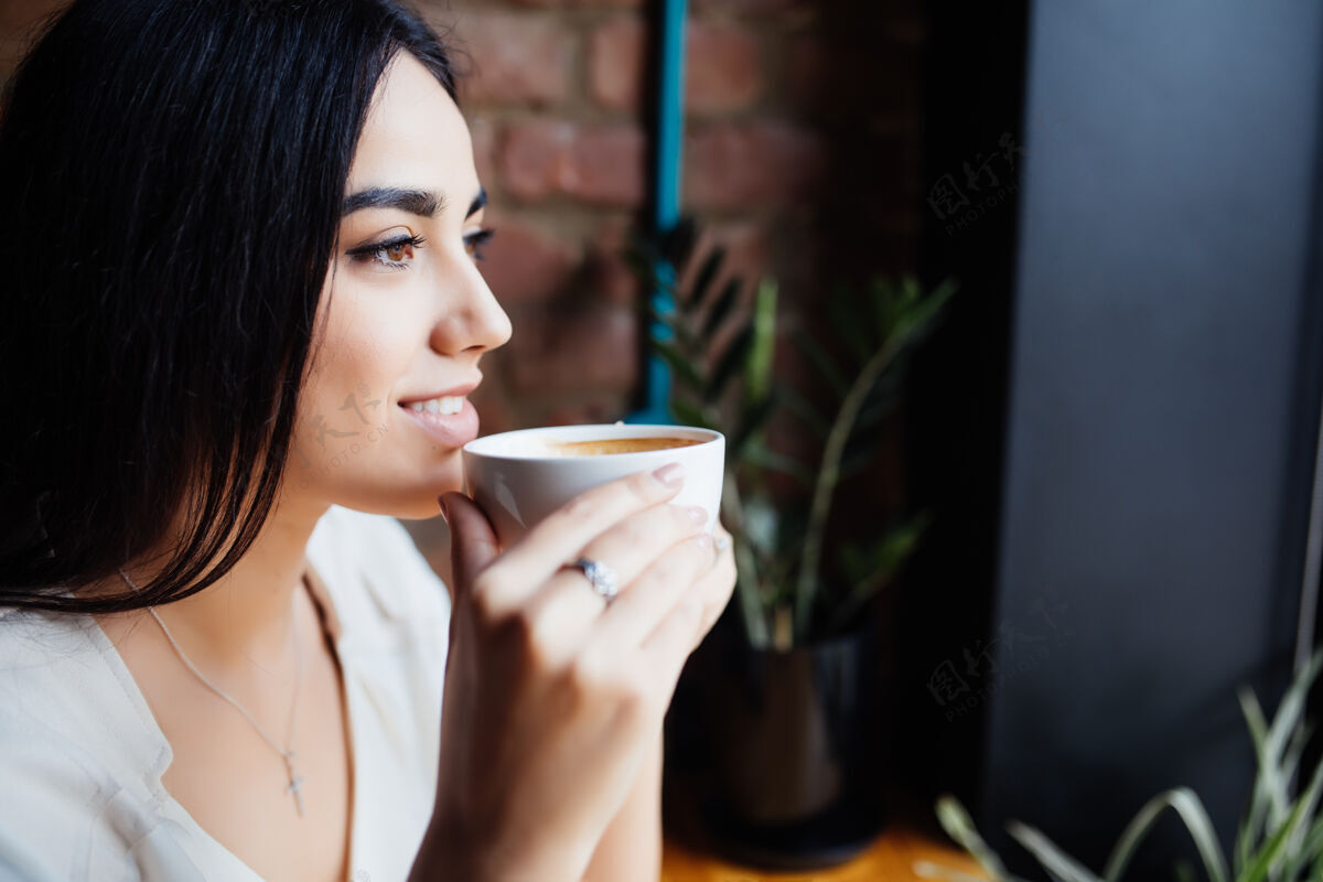 早晨咖啡美女在咖啡厅喝茶或咖啡美女模特用一杯热饮料暖色调室内女士咖啡馆