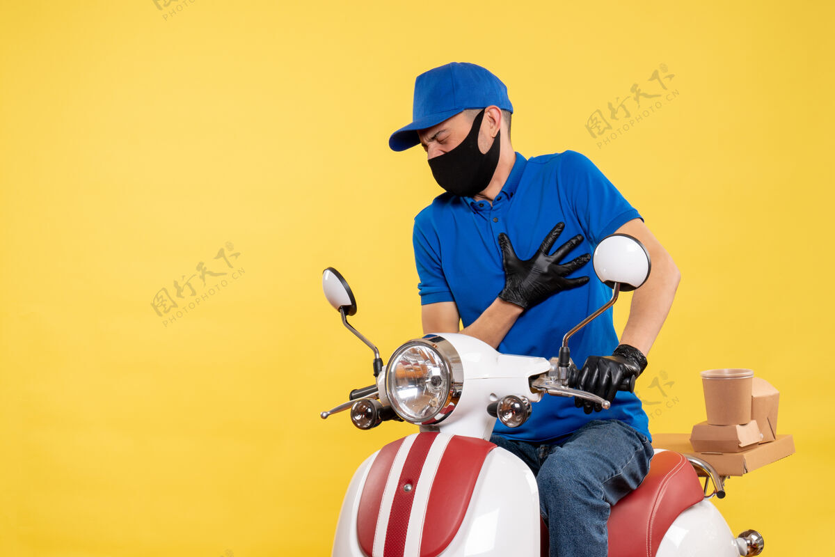 男人正面图身穿蓝色制服的年轻男性快递员在黄色背景上covid-大流行性服务工作病毒自行车工作递送痛苦摩托车车辆黄色