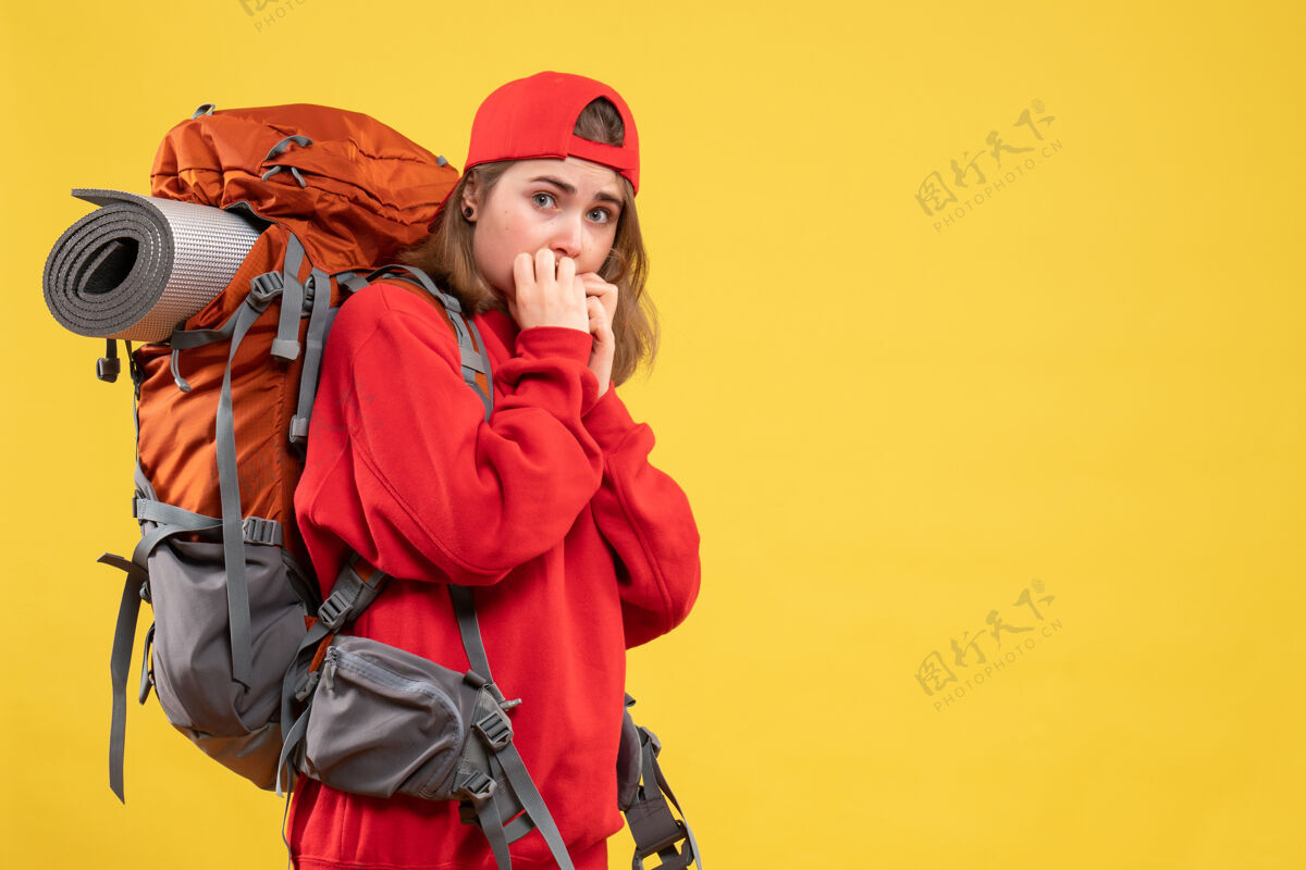 前面黄色墙壁上穿着红色背包的忧心忡忡的旅行者妇女害怕背包帽子
