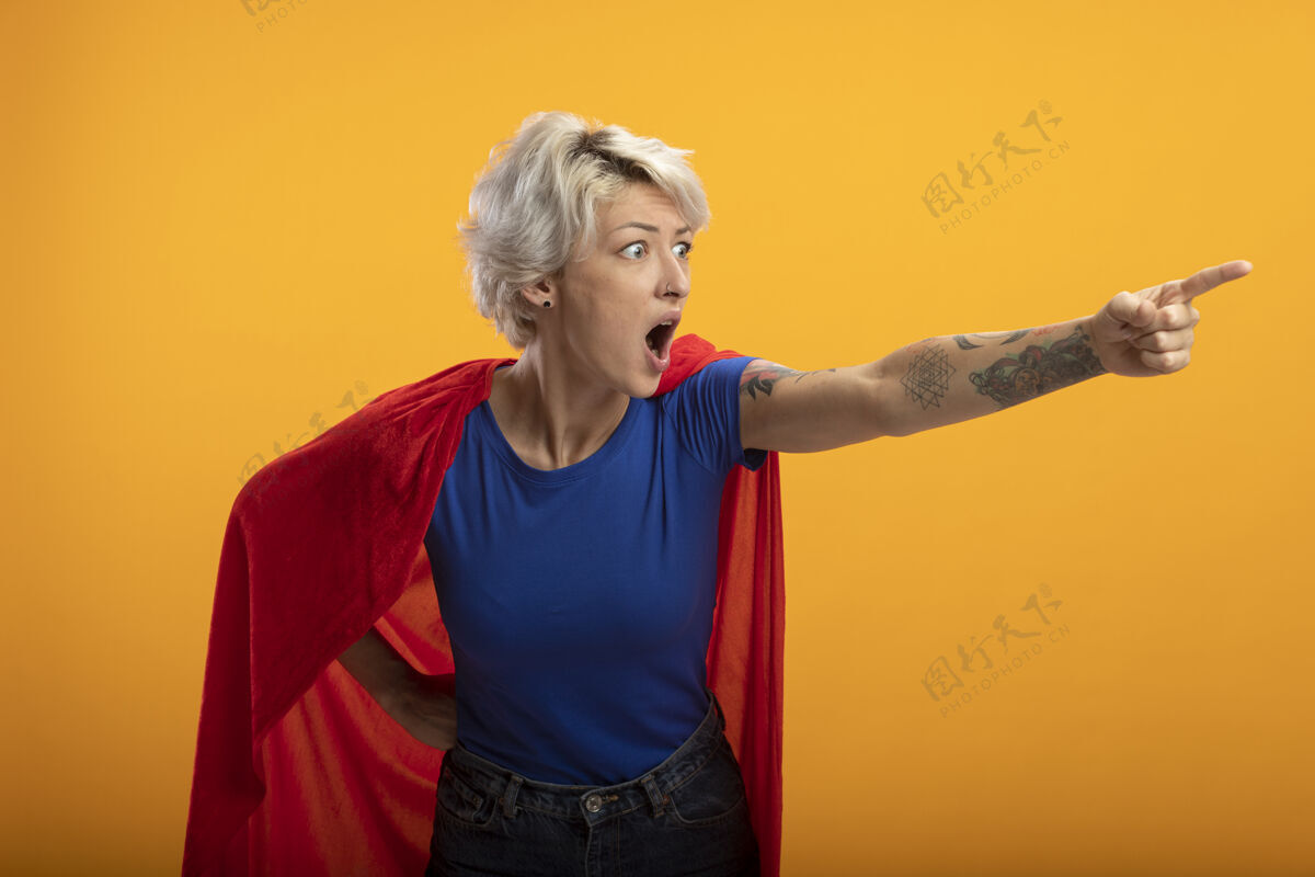 超级英雄穿着红色斗篷的震惊女超人看着橙色墙壁上孤立的一面公民女人姿势