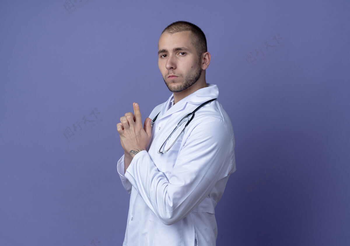 衣服自信的年轻男医生 身穿医用长袍 脖子上戴着听诊器 站在侧视图中 用手做着的手势 看着紫色墙壁上孤立的前方医学手势男性