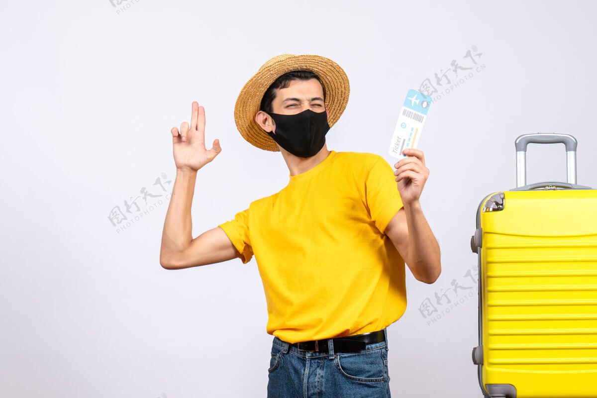 手提箱正面图穿着黄色t恤的年轻人站在黄色手提箱旁举着旅行票制作手指枪前面手持手指
