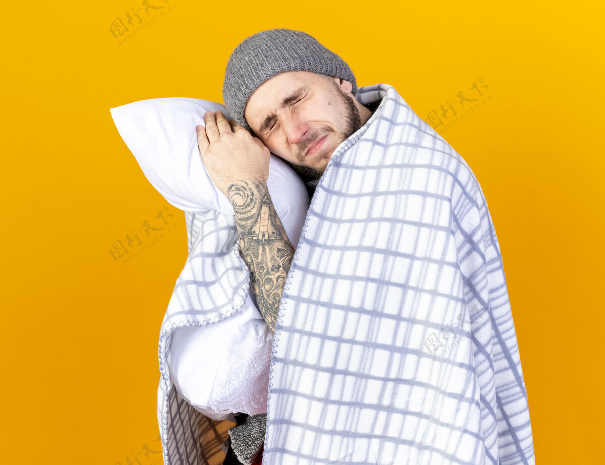 帽子一个戴着冬天帽子 围着方格布围巾的年轻病夫把头靠在隔离在橙色墙上的枕头上格子市民男人