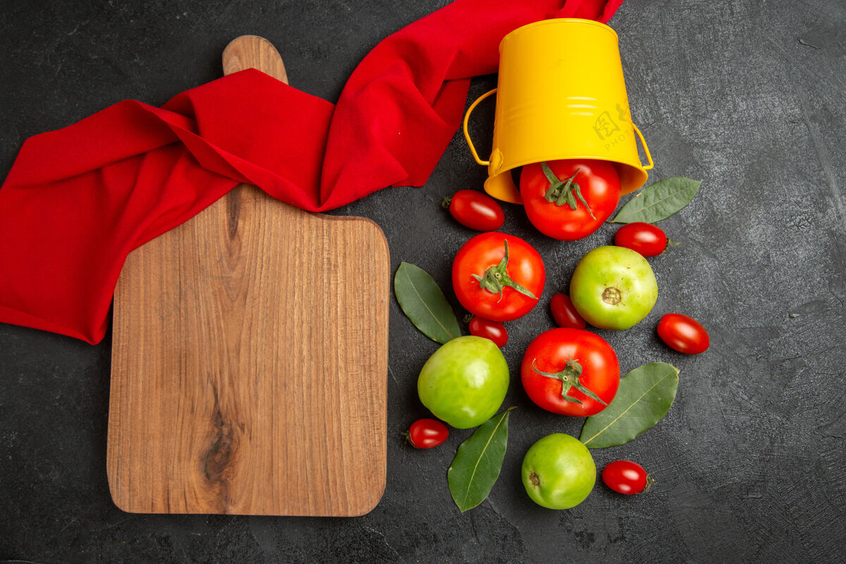 番茄顶视图桶与红绿色和樱桃番茄湾叶红毛巾和砧板上的深色背景海湾蔬菜叶