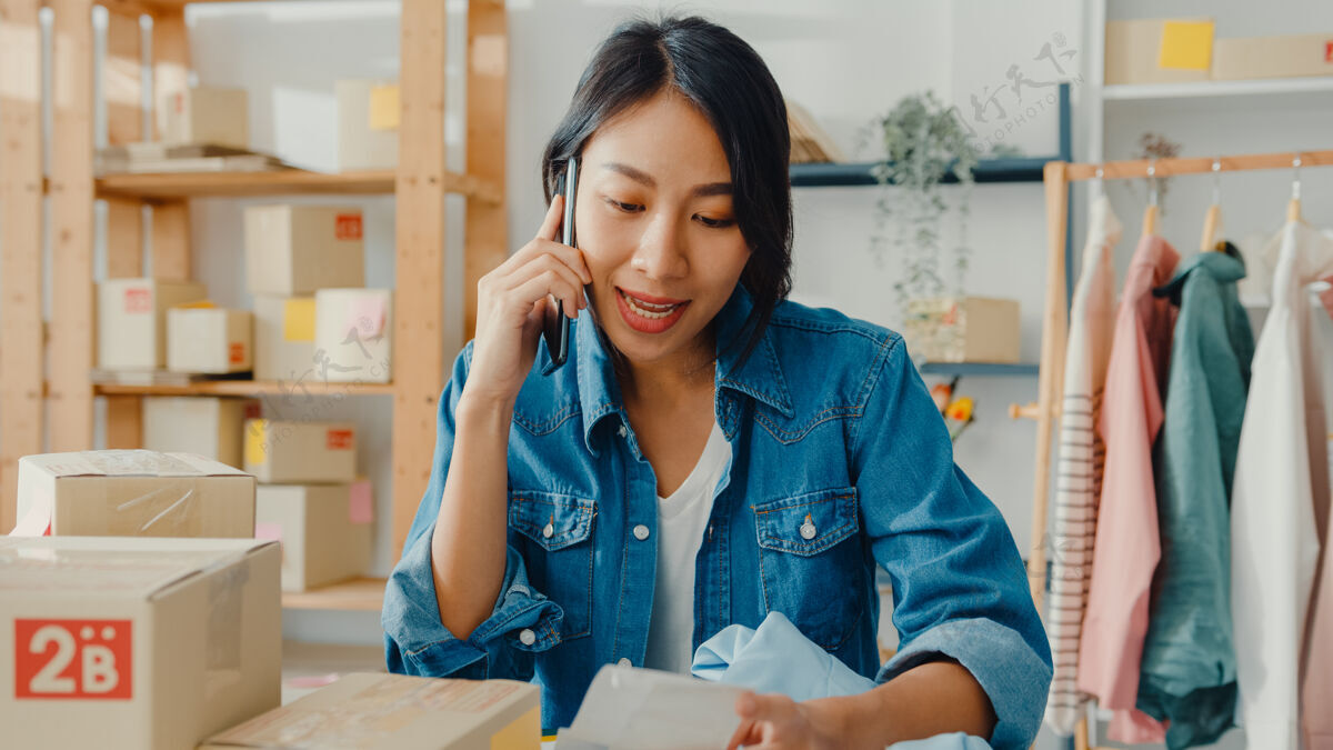 服装年轻的亚洲女商人使用智能手机接收采购订单 并检查产品的库存工作在家里的办公室工作客户支票