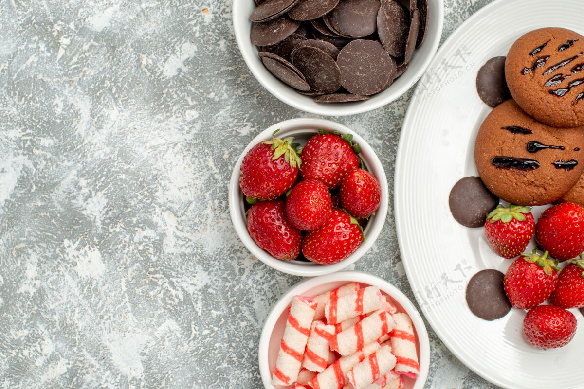 食品顶部近距离观看白色椭圆形盘子上的巧克力饼干草莓和圆形巧克力 灰白色地面上的碗里有糖果草莓巧克力巧克力椭圆形农产品