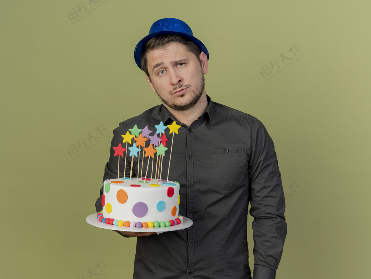 绿色悲伤的年轻人穿着黑色衬衫 戴着蓝色帽子 拿着橄榄绿的蛋糕派对年轻戴着