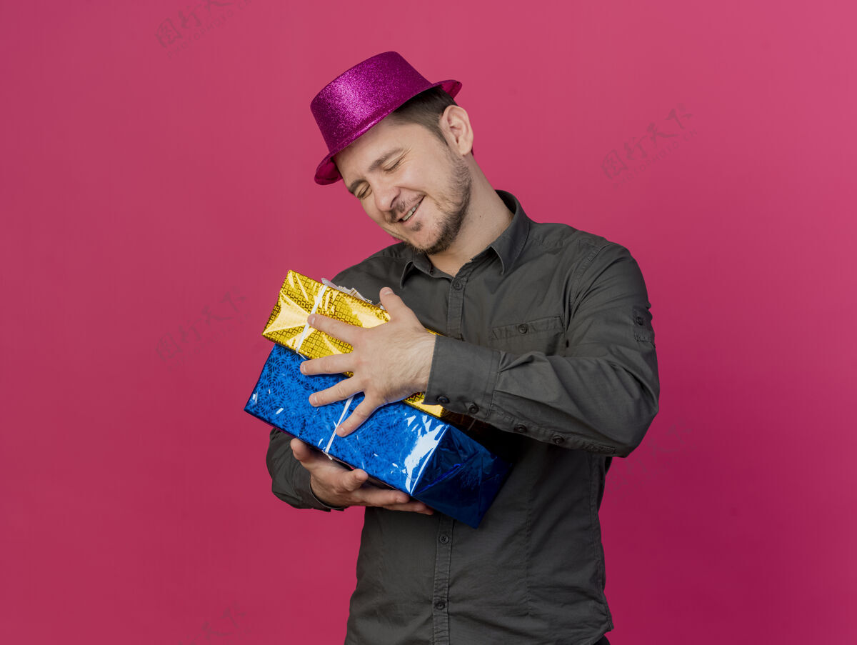 礼物高兴的年轻人闭着眼睛戴着粉红色帽子拥抱礼品盒孤立的粉红色年轻盒子粉色