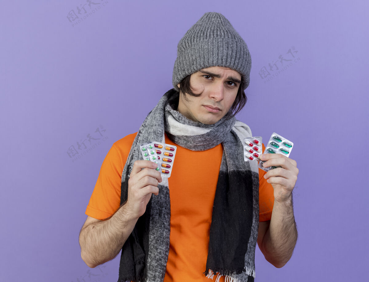 帽子悲伤的年轻人戴着冬天的帽子 戴着围巾 手里拿着紫色隔离的药丸药丸生病年轻