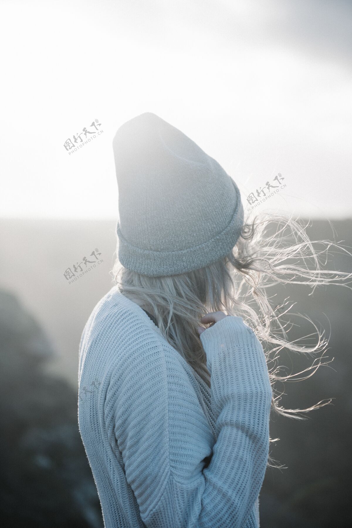 时尚一个年轻的金发女人戴着帽子在沙滩上走在一个刮风的天气背景海岸女性