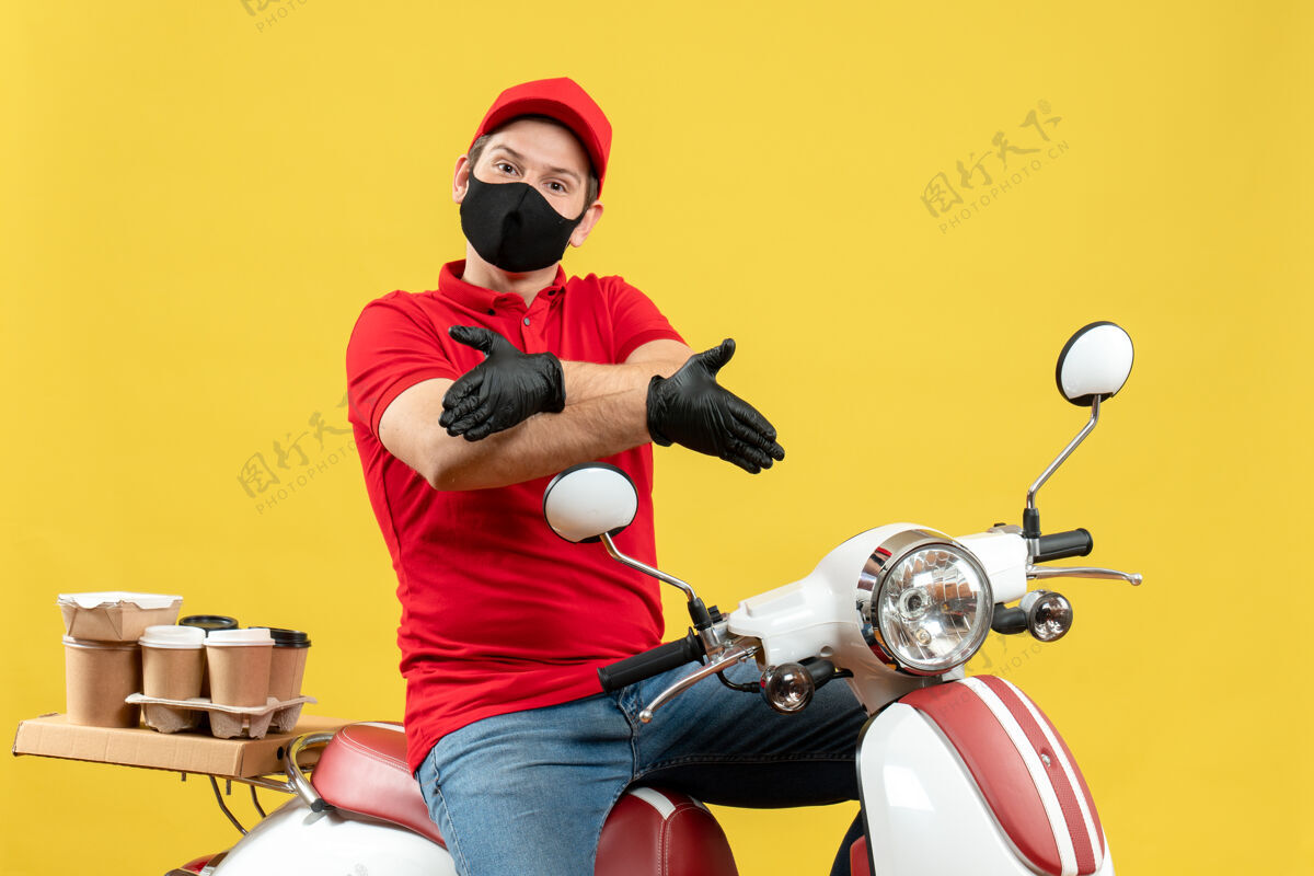 年轻人俯视图：情绪激动的年轻人穿着红色上衣 戴着帽子 戴着手套 戴着医用口罩 传递着命令 坐在踏板车上欢迎某人车辆摩托车交付